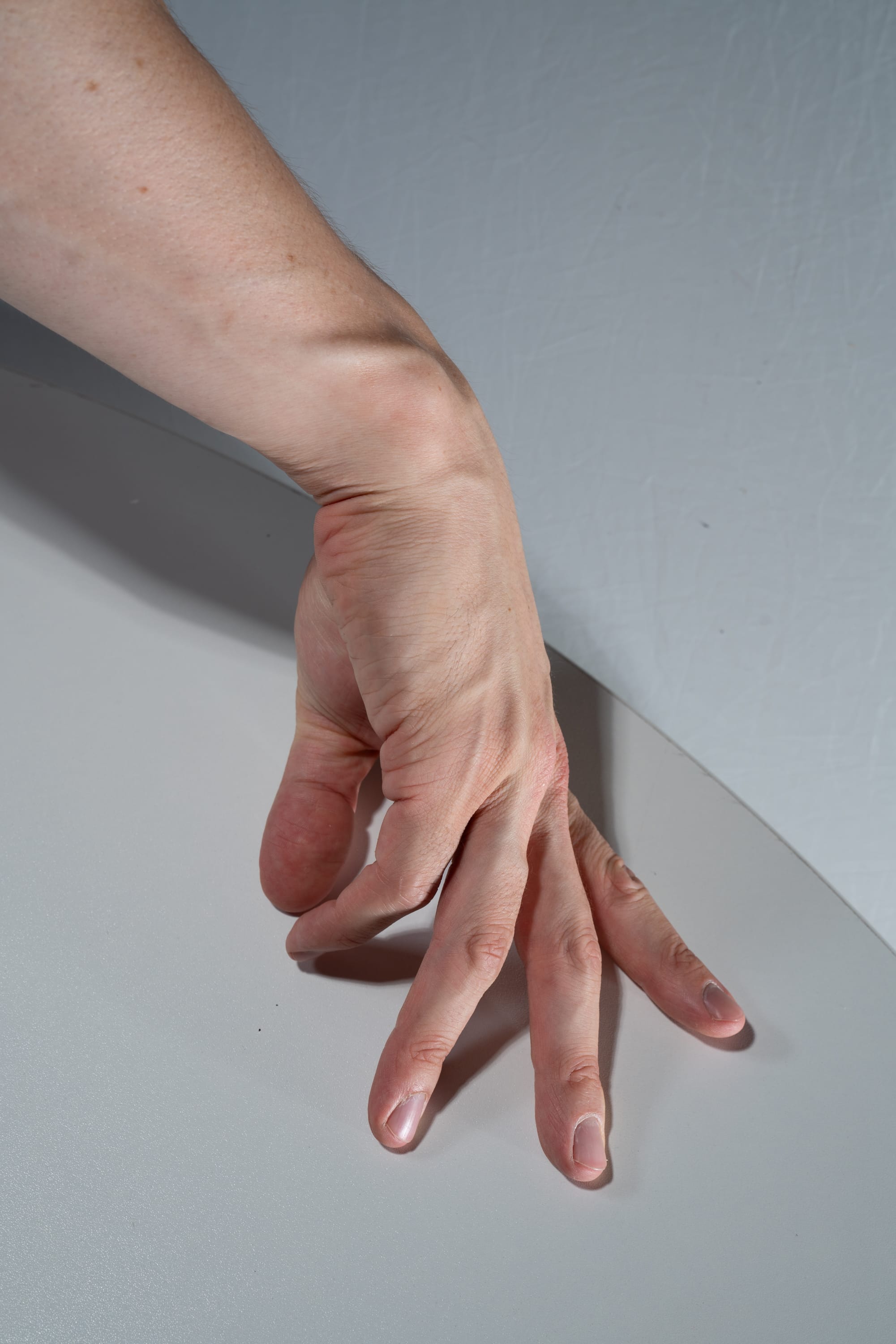 a caucasian hand and lower arm are shown with fingers curled inward, like the hand is about to grip something. the hand rests on a white table.