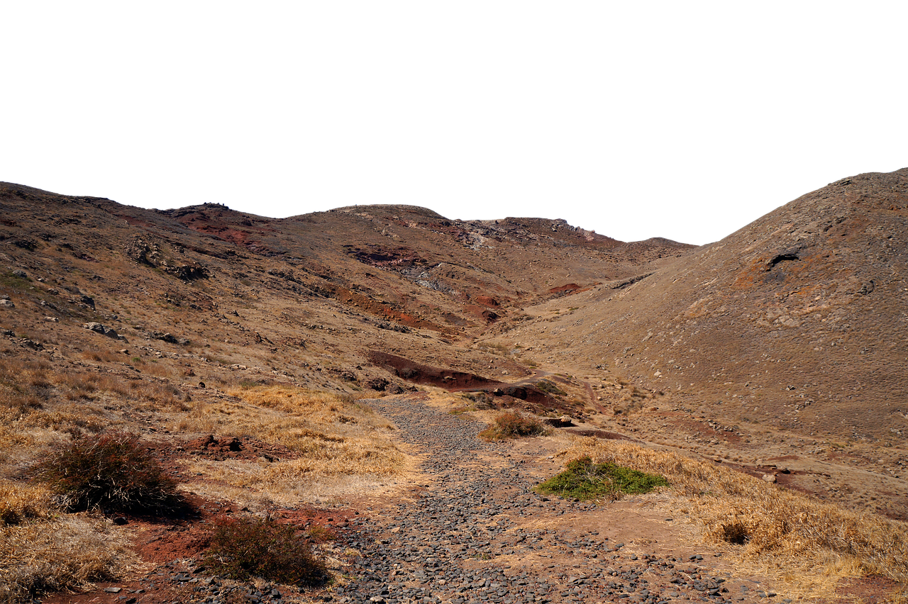 a desert landscape with a rocky path leading through arid terrain. the scene includes mountains, shrubs, red soil, and dry grass. the sky is blacked out.