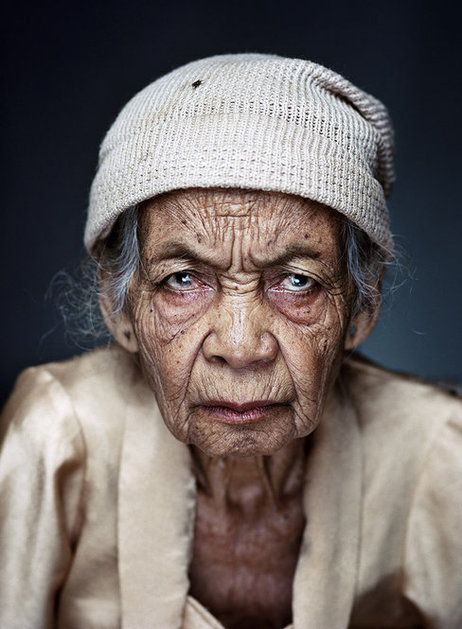 a closeup portrait of an elderly woman with a serious and intense expression. she is wearing a white beanie, and her face shows many wrinkles, highlighting her age. the photo captures the details of her skin texture and the depth of her eyes.