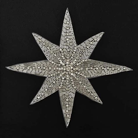 the image shows a silver, eightpointed starshaped patch adorned with small crystals and beads. the patch is placed on a black background.