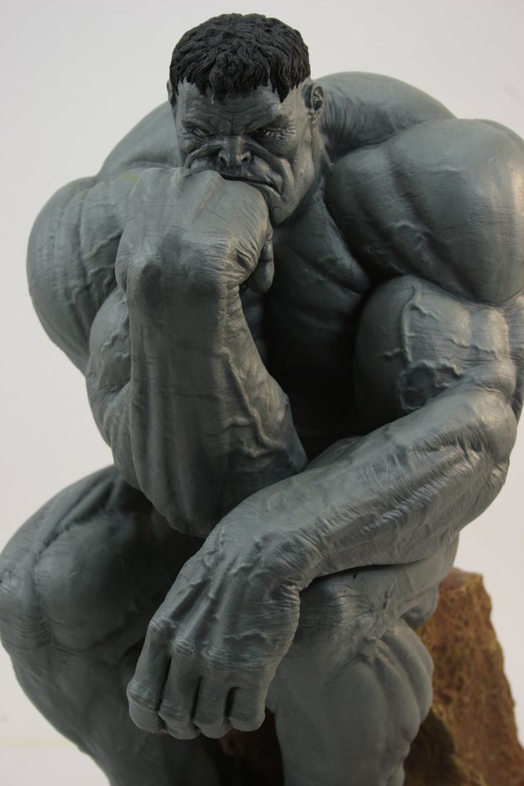 a gray sculpture of the hulk, posed in a contemplative position reminiscent of rodin's "the thinker." he sits with his chin resting on his fist, his brow furrowed in thought. the sculpture highlights his muscular physique and powerful presence. the background is a plain white, suggesting a studio setting.