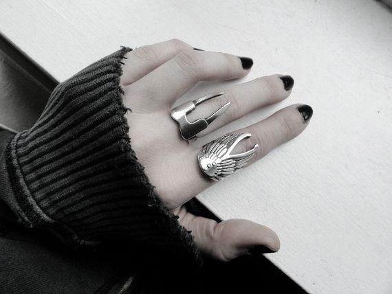 a hand with black nail polish wearing two metal rings. the person is wearing a dark sweater.