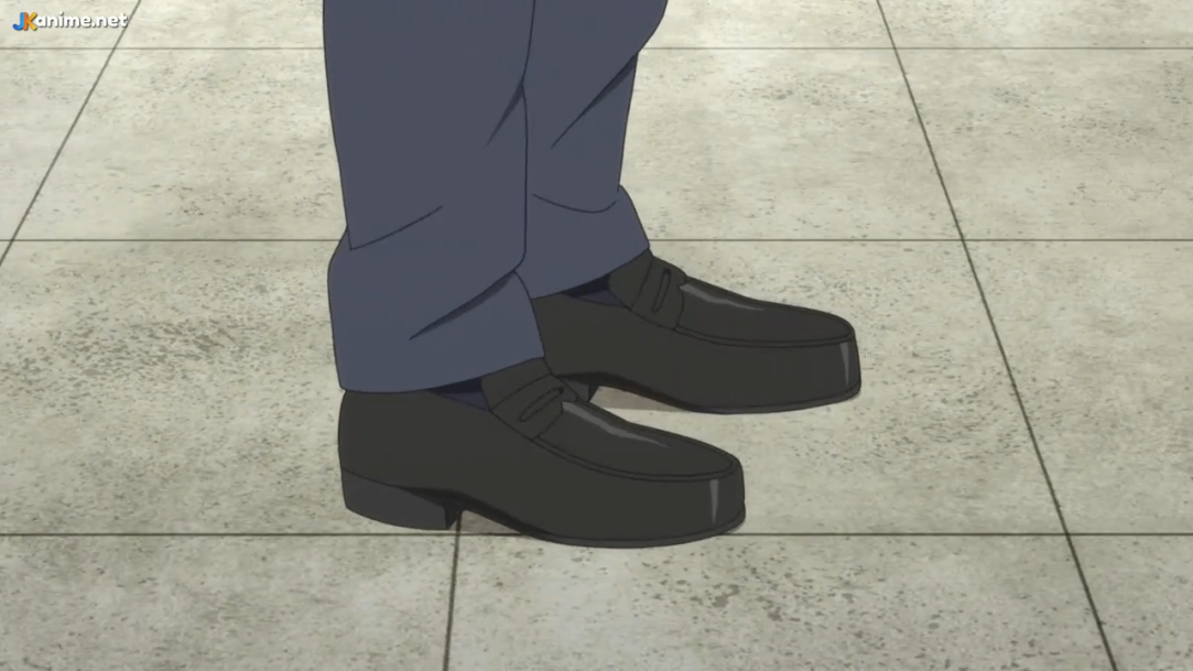 a man in business casual attire stands on a beige tiled floor. the focus is on his lower body, specifically his black dress shoes and dark blue pants. the lighting is bright, likely artificial, and the perspective is from a high angle.