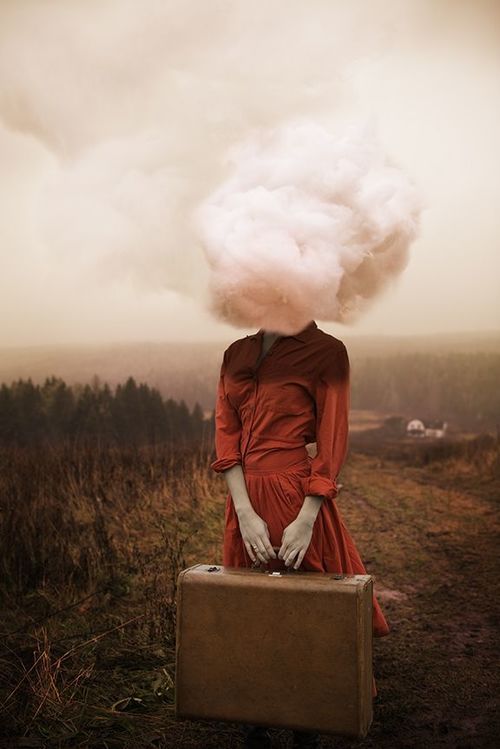 a surreal and artistic image featuring a woman standing outdoors in a sepiatoned landscape. the woman is wearing a red dress and holding a brown suitcase. in place of her head, there is a large, fluffy cloud. the background includes a field, hills, and trees, creating a mysterious and dreamlike atmosphere.