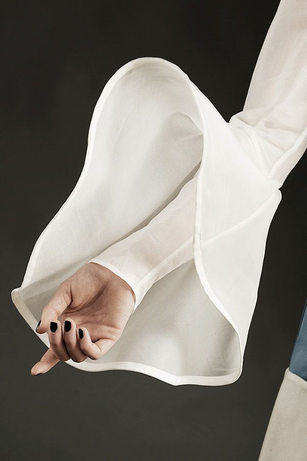 closeup image of a hand with black painted nails peeking out of a white, sheer blouse sleeve.