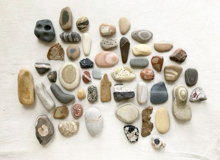 a collection of smooth, assorted rocks and stones on a white surface.  the rocks are gray, beige, brown, and white, and some have interesting patterns and textures.  they are spread out in an organized, slightly overlapping manner on the surface.
