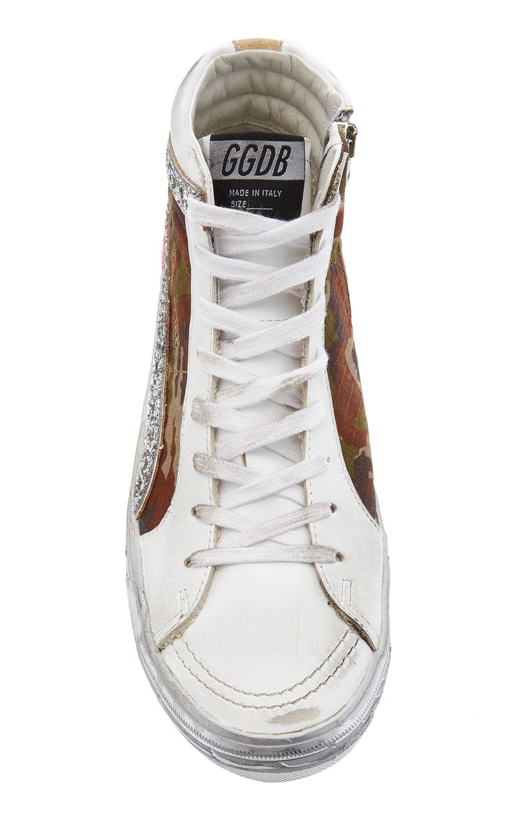 a topdown closeup shot of a pair of golden goose ggdb hightop sneakers. the sneakers are white leather with a camouflage print on the heel and sides. there is glitter detailing along the sides. the sneakers appear to be distressed, giving them a worn look. the ggdb logo is visible on the tongue.  the shoes are made in italy.