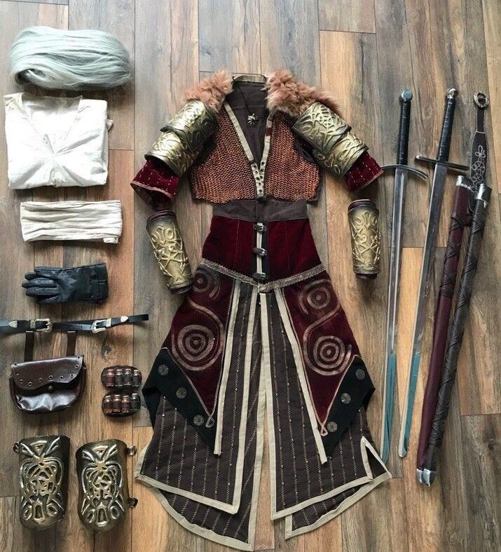 a laid out outfit on a wooden floor consists of a costume including: a large pile of white fiber, a white shirt, a tan band of cloth, a black glove, a leather belt with a small pouch, small pouches on a strap, gold boot armor, upper body armor with gold shoulder and arm guards and a brown chainmail vest with fur around the neck, a long skirt with a red top and brown panels, a long sword, and a sword in a scabbard.