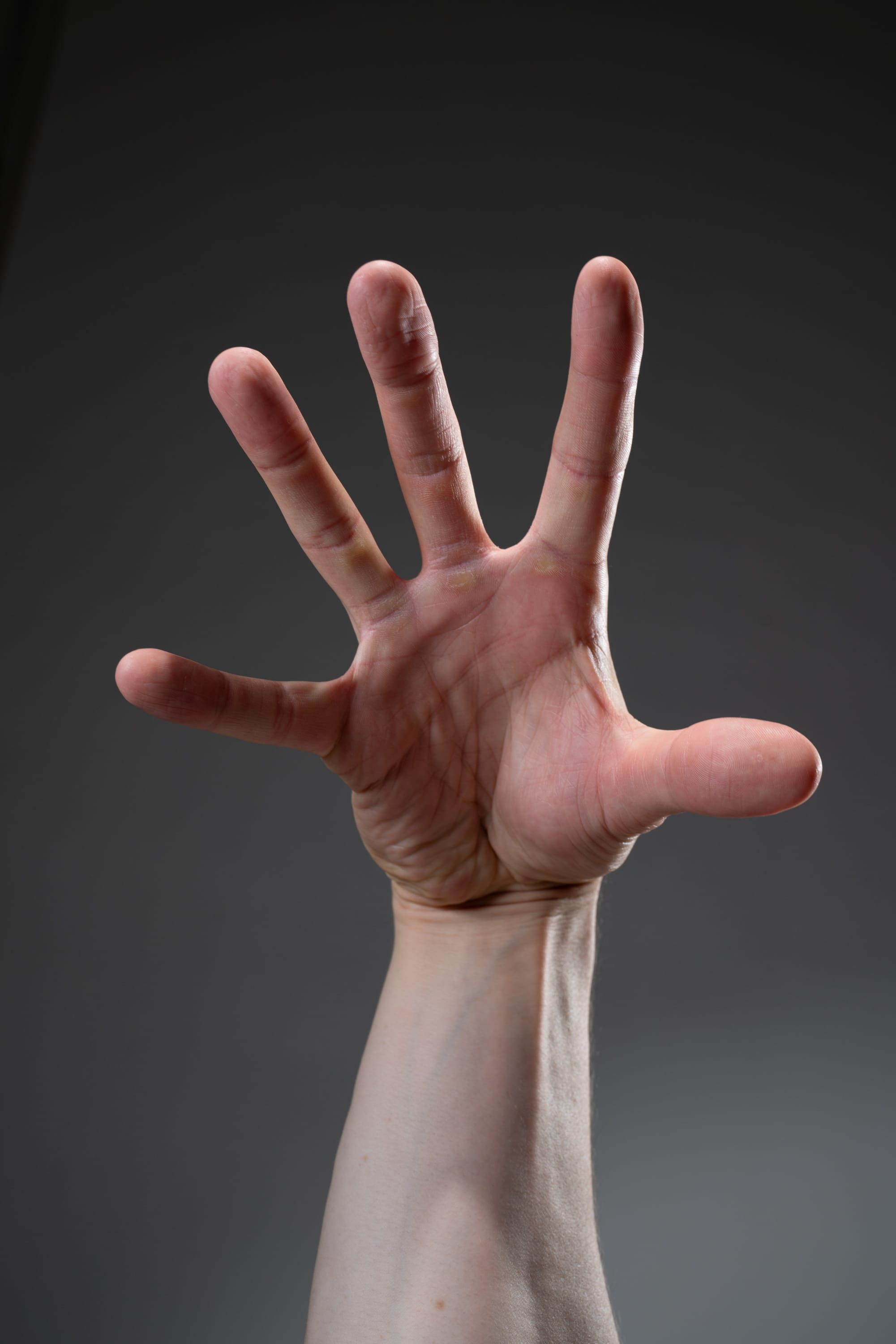 a closeup image of a man's open hand against a neutral gray background. the hand is outstretched with all five fingers extended, creating a gesture that suggests reaching out, offering, or signaling a stop.
