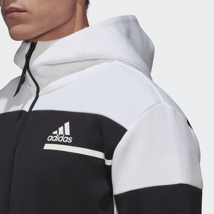 a closeup shot of a man wearing a white and black adidas hoodie. the hoodie has a zipper closure, a black adidas logo, and white stripes. the man is wearing a black shirt underneath the hoodie.