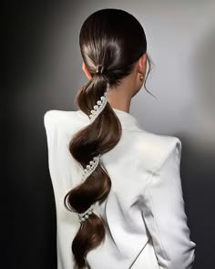 a bride with her long brown hair pulled back in a ponytail adorned with pearls. she is wearing a white jacket.  the image is taken from the back and focuses on her hairstyle.