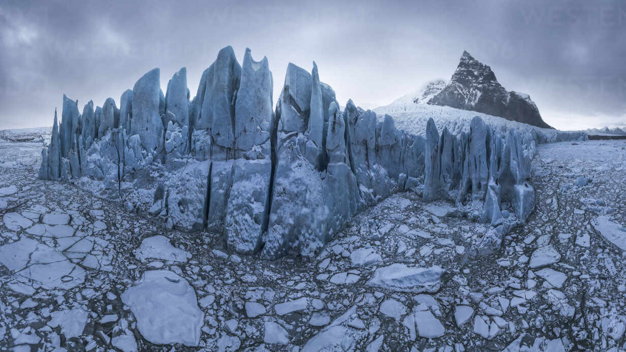 a stunning aerial view of a glacier in iceland. the glacier's surface is a patchwork of ice and snow, with large cracks and crevasses. in the distance, a snowcapped mountain rises up against a cloudy sky. the scene is both beautiful and aweinspiring, capturing the power and fragility of nature.