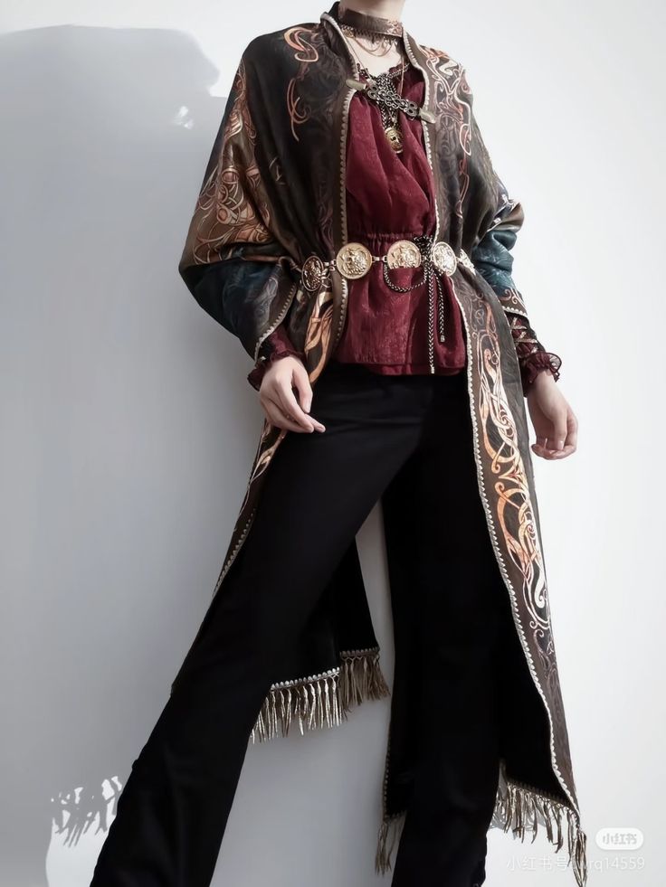 a full shot of a woman standing in an outfit. she is wearing black pants with an open brown duster with decorative brown and gold designs, and a maroon blouse underneath the duster. she has a gold belt around her waist. she also wears a choker and a necklace. the clothing is gothic and vintageinspired.