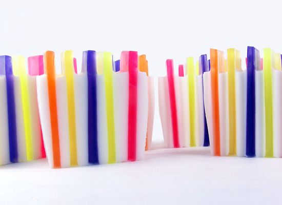 a close up photo of four bars of soap in rainbow colors. the soap bars are stacked in a row, from left to right.  the soap bars are all white with rainbow colored stripes. the soap bars are on a white background.