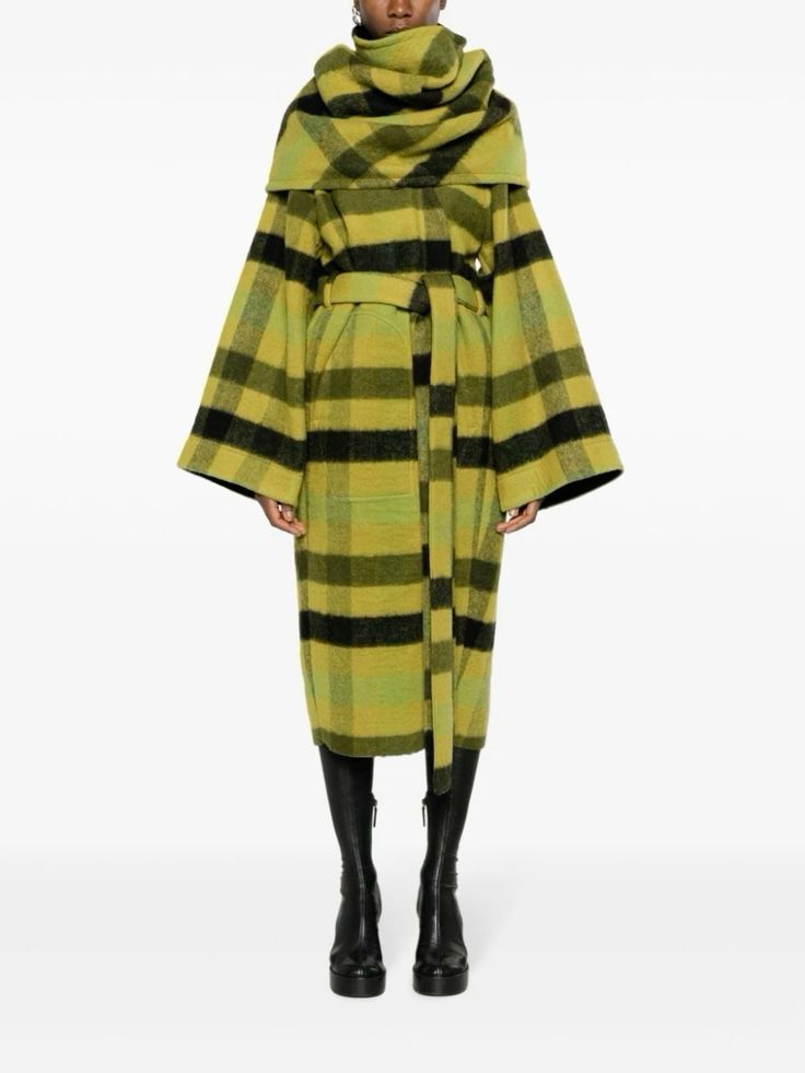 a woman wearing a green and black plaid coat with a wide collar. she is wearing black boots and looks stylish and chic. the coat is a long, flowing style that would be perfect for fall or winter.
