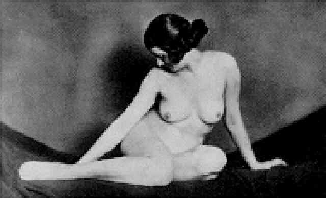 the image is a black and white photograph of a nude woman seated.  she is positioned with her body slightly turned away from the viewer, her head bowed, giving a sense of introspection or melancholy. her pose is relaxed yet elegant, and her body is softly lit, with shadows creating depth and contrast. the background is dark and unfocused, drawing attention to the subject. the style suggests a vintage photograph, possibly from the 1920s or 30s, reflecting the aesthetics of the era. the overall mood is quiet and suggestive rather than overtly provocative.