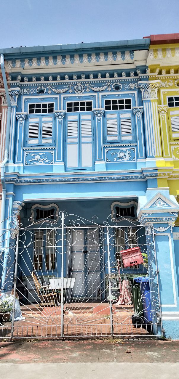 a blue building with ornate windows, a wrought iron gate, and a colorful building next to it. the building is located in singapore and is an example of traditional southeast asian architecture.