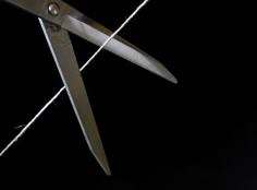 a pair of scissors with one blade open and the other closed, with a needle intersecting the blades. the scissors and needle are against a black background.  the image is likely symbolic of cutting or separation.