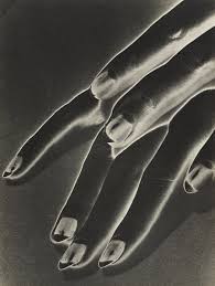 the image is a striking closeup monochrome photograph of a hand.  the style is highly evocative of surrealist and experimental photography, possibly a photogram given the high contrast and almost ethereal quality of the image. the fingers are elongated and slightly distorted, creating an almost abstract representation of the human hand. the lighting emphasizes texture and shadows, highlighting the curves and contours of the skin and nails. the overall effect is one of both beauty and mystery, with the image’s ambiguity lending itself to various interpretations.