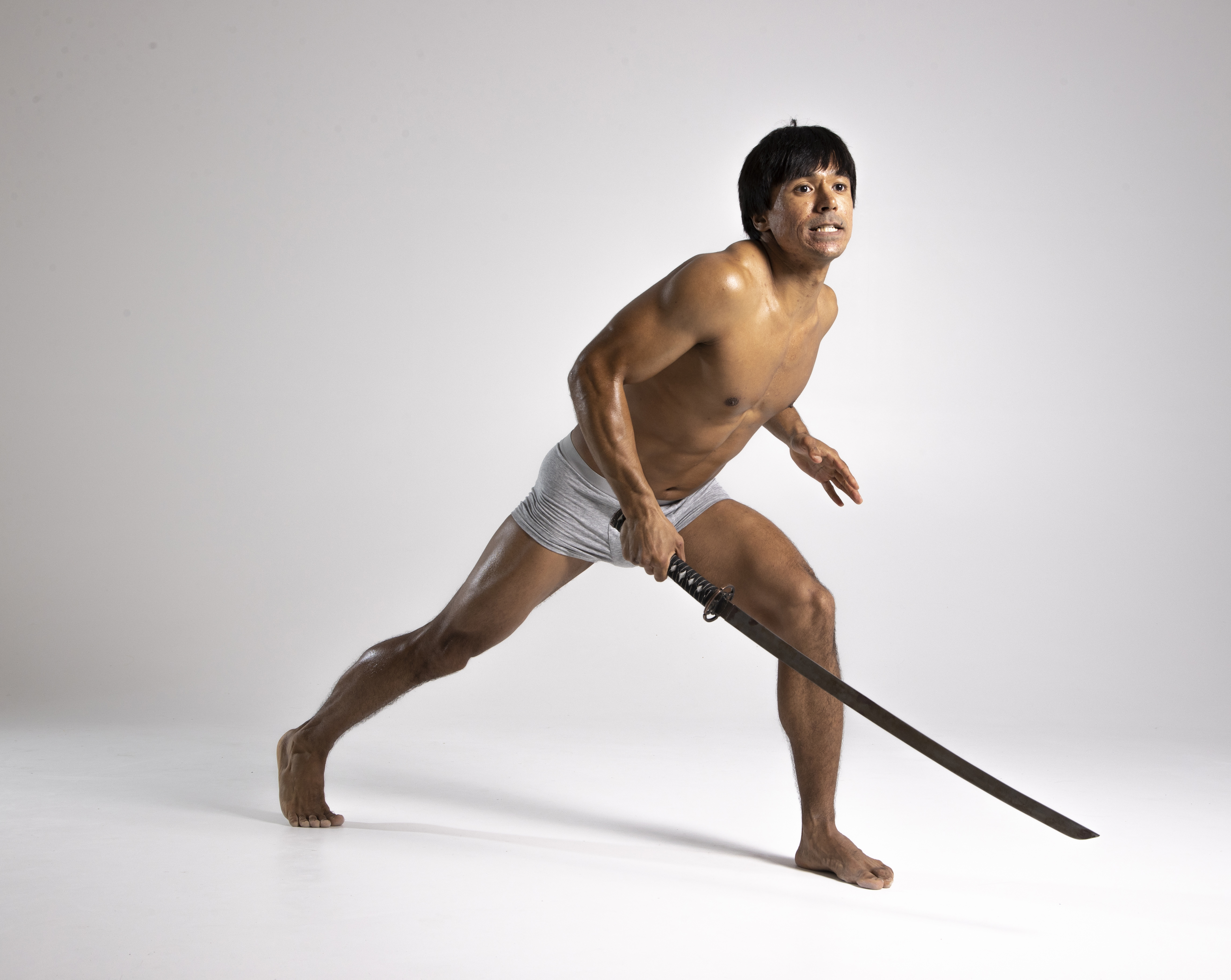 a shirtless man in gray briefs stands on a white background holding a sword. he is barefoot and appears to be in a fighting stance.