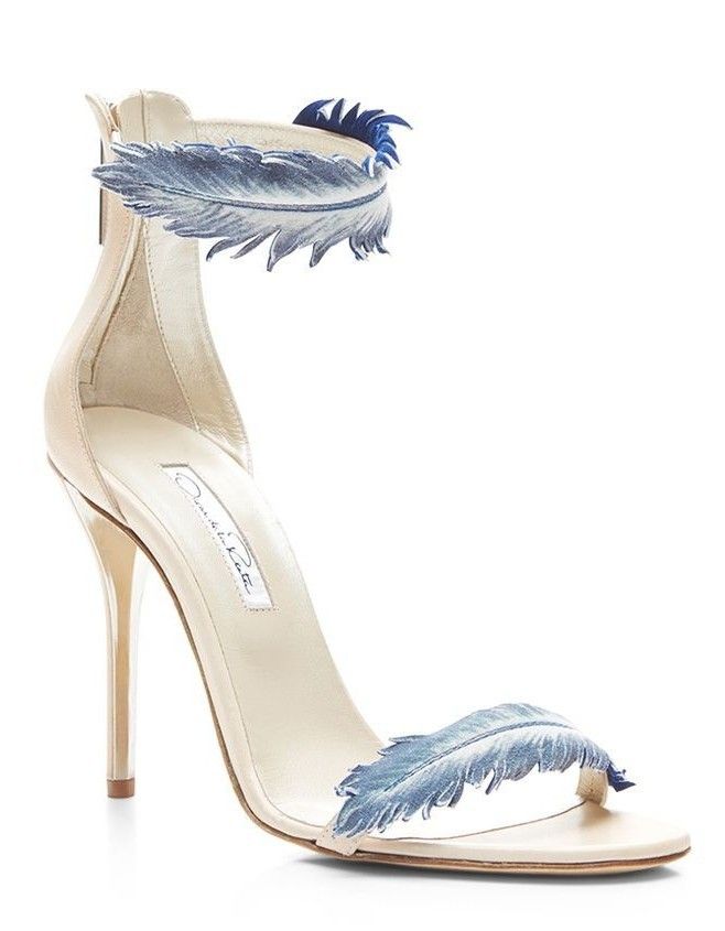 a pair of white high heel sandals with a blue feather embellishment on the ankle strap and toe strap. the sandals have a stiletto heel and are made of leather. they are a great choice for summer and are perfect for dressing up any outfit.