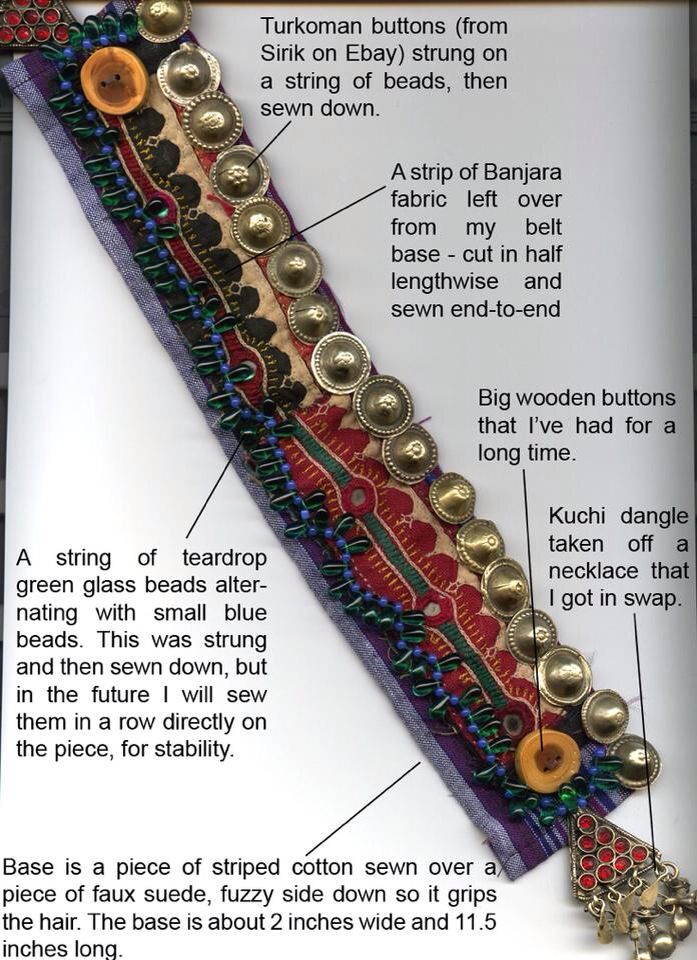 a closeup image showcasing the details of a handmade hairpiece or accessory. the base is made of striped cotton sewn over faux suede. adornments include turcoman buttons strung on beads, a strip of banjara fabric, teardrop green glass beads alternating with small blue beads, wooden buttons, and a kuchi dangle. the various elements are sewn onto the base.