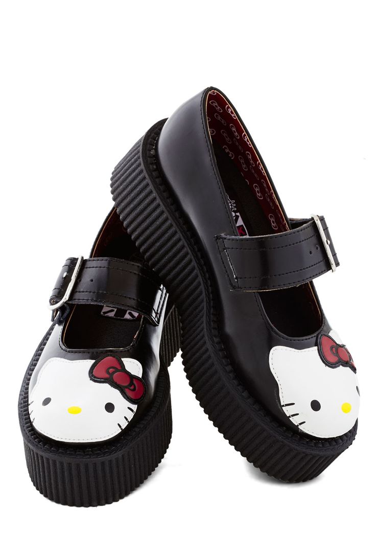 a pair of black platform creeper shoes with hello kitty designs are displayed. the shoes are angled towards each other on a white background. the shoes feature a black strap with a buckle, and the front of the shoe has a white hello kitty face with a red bow. the thick, ridged platform sole is visible. the inside lining has a pattern with hello kitty images.
