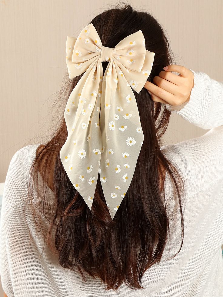 a young woman with long brown hair is modeling a beige hair bow with a small white daisy print. the bow is tied at the crown of her head with long tails that fall down her back. the background is a pale pink wall.