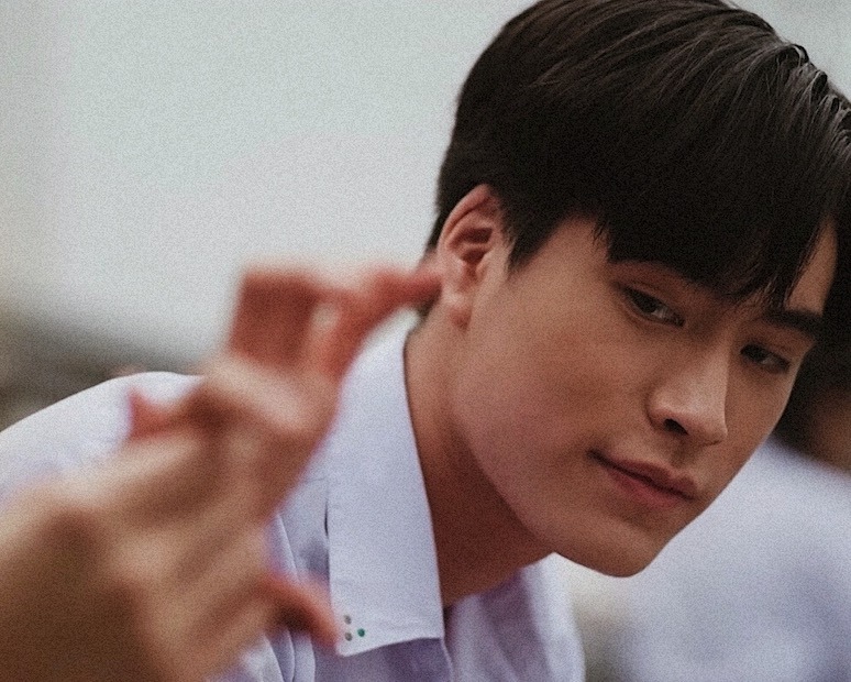 a closeup portrait of a young asian man with a contemplative expression. he is wearing a white collared shirt and his dark hair is styled in a fringe. the background is blurred, suggesting an outdoor setting. the lighting is soft and natural, casting a gentle glow on the subject's face. the overall mood of the image is serene and introspective.
