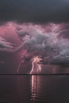 a dramatic shot of a stormy sky above a body of water. the sky is filled with dark, ominous clouds with flashes of lightning illuminating the scene. the water is still and reflects the storm clouds and lightning above. the image has a moody and atmospheric feel to it.