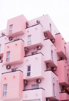 a close up of a modern pink apartment building with balconies and air conditioners. the building has a clean and simple design with white trim around the windows. the pastel pink color is soft and inviting, making the building look elegant and sophisticated. the balconies are spacious and provide residents with a view of the city. the air conditioners are modern and blend seamlessly with the building's design. the overall effect is a modern and stylish building that is both functional and aesthetically pleasing.