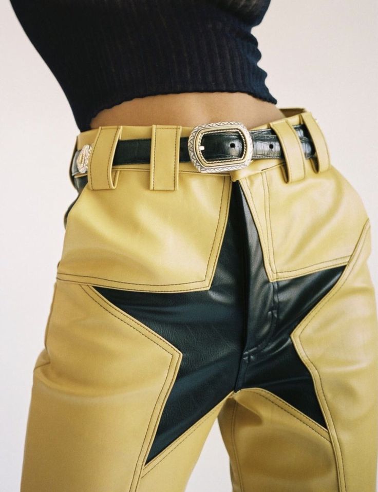 a woman wearing a black sweater and a pair of yellow and black leather starshaped pants with a silver belt buckle is standing in a casual pose.