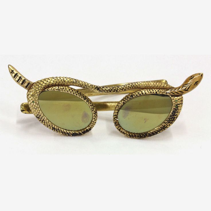 the image shows a pair of goldcolored sunglasses styled as a snake. the frame of the glasses is designed to resemble the body of a snake, with the head and tail forming the ends of the frame. the lenses are ovalshaped and appear to have a reflective surface. the snake design features scales and detailed features, giving it an ornate, antique appearance. the overall style of the sunglasses is fashionforward and unique.