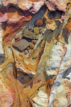 a closeup view of a rock face with intricate patterns and textures. the rock is composed of various shades of brown, yellow, orange, and gray. the surface is weathered and eroded, creating a rough and uneven texture.  the patterns in the rock suggest layers of different mineral deposits.  the rock appears to be a mixture of different types of stone, creating a fascinating natural abstract art piece.
