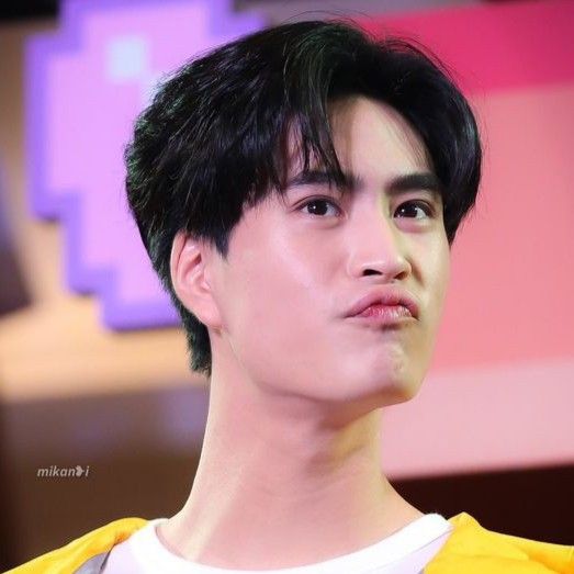 a closeup portrait of a young asian man with short, dark hair. he has a pleasant expression on his face, with his lips slightly parted. the lighting is soft, giving his skin a warm glow. he is wearing a yellow and white shirt. the background is blurred, but appears to be an indoor setting.