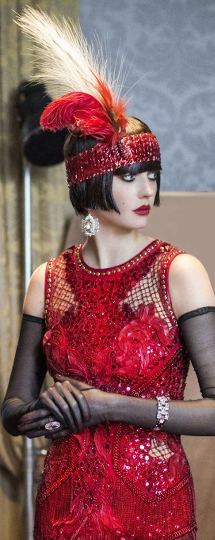 a glamorous woman in a red flapper dress and a feathered headband. she is wearing black gloves and jewelry and has her hair styled in a bob.