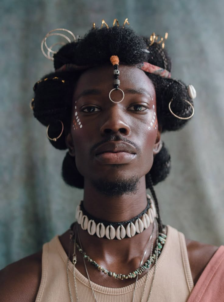 a portrait of a man with dark skin and a beard, wearing traditional attire including an afro hairstyle adorned with beads, rings, and a shell choker. he has face paint, and is wearing a beige tank top with necklaces. the background is a mottled green and blue.
