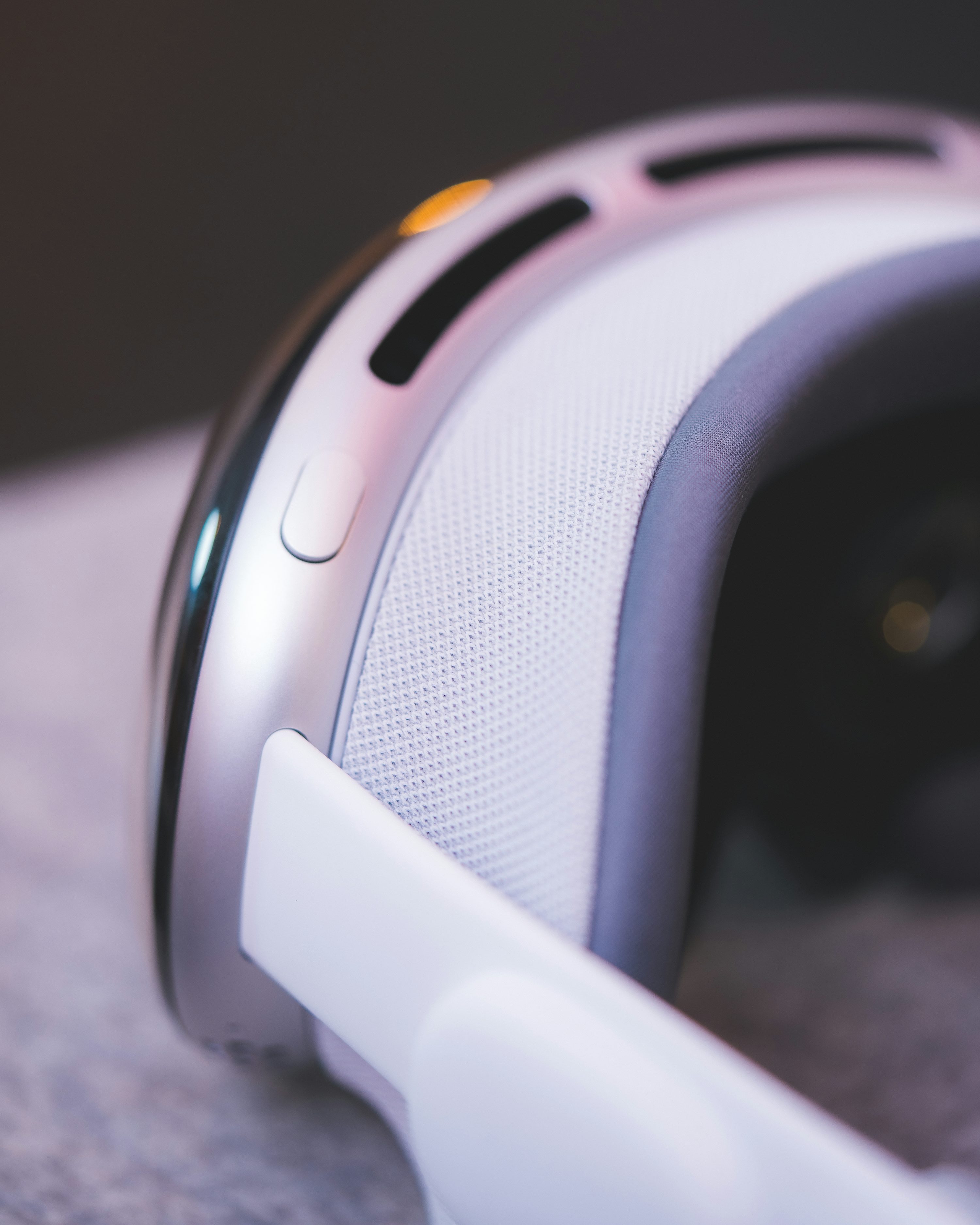 a closeup shot of a vr headset, showcasing its sleek silver and white design. the image focuses on the details, including the button, strap, vents, and the overall futuristic aesthetic of the device.