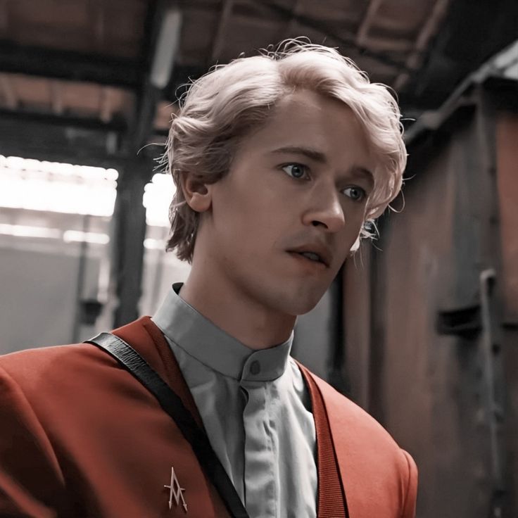 a close up portrait of a handsome blonde man in a red jacket and white shirt, standing in a dark urban environment. he is looking intensely at something offcamera. the lighting is dramatic and creates a sense of mystery.