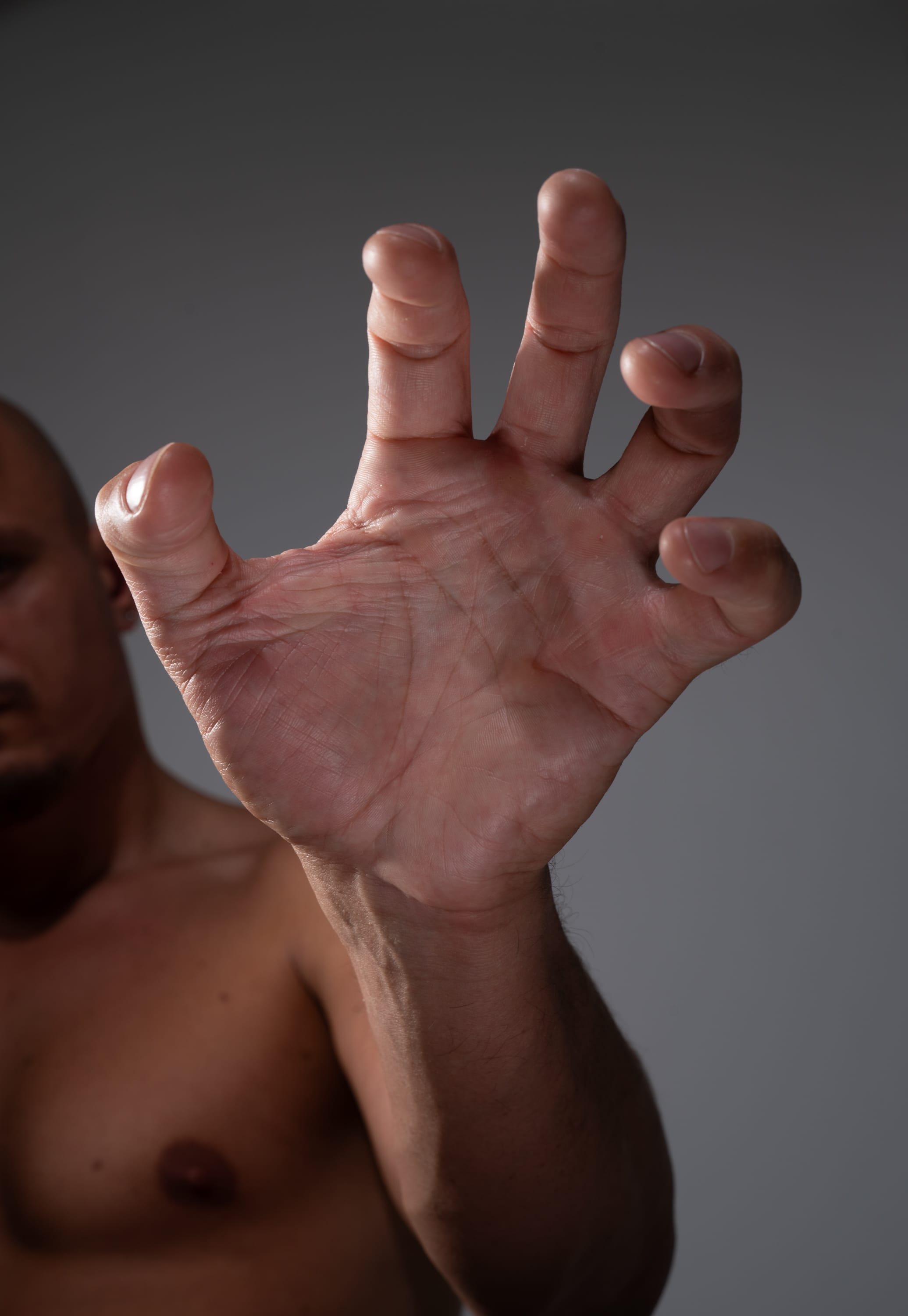 a closeup of a man's outstretched hand, fingers curled as if reaching or grabbing for something.  the man's face and upper torso are partially visible, creating a sense of intimacy and focus on the hand gesture. the soft, natural lighting emphasizes the details and textures of the skin.