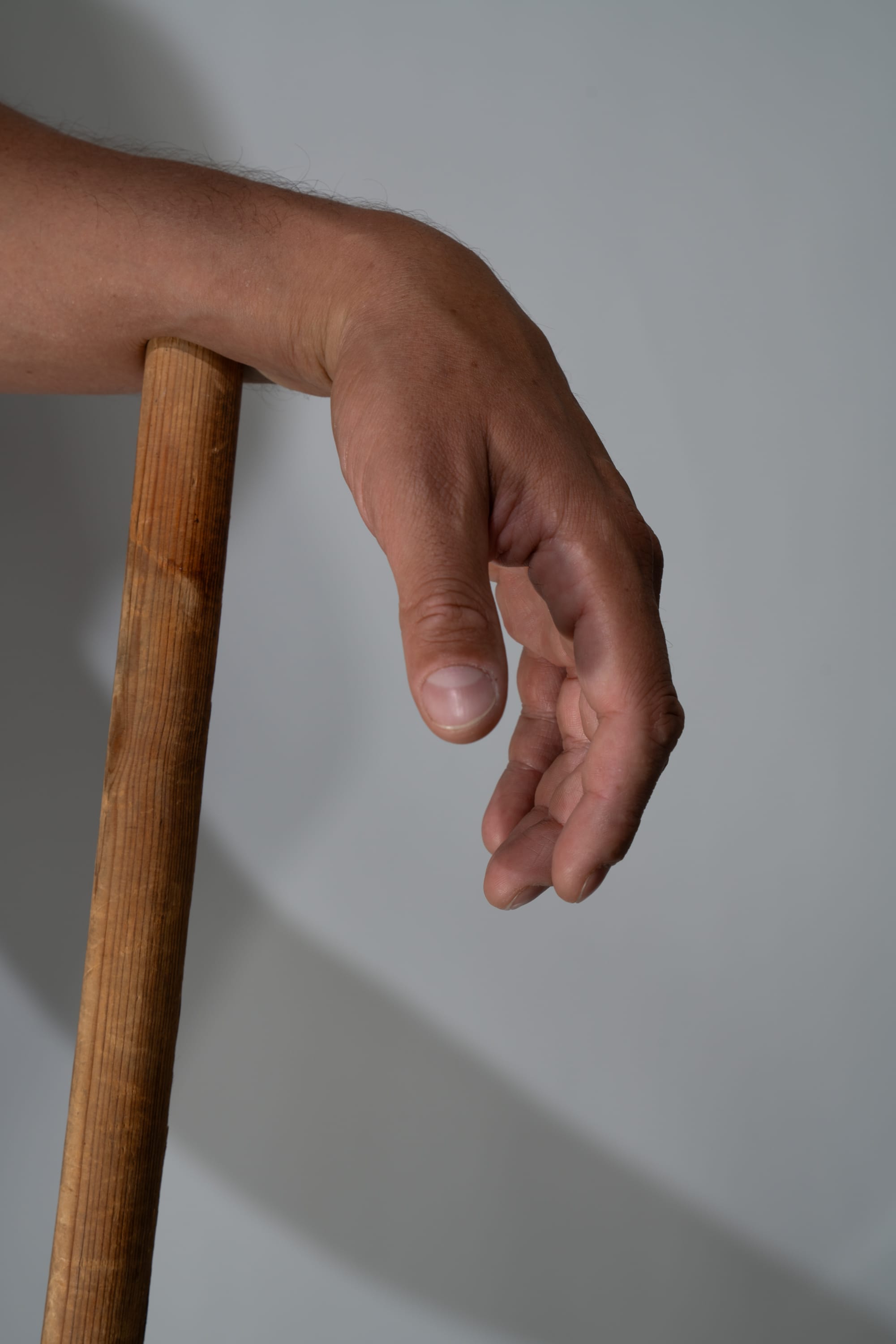the image shows a closeup of a person's hand and arm resting on a wooden pole. the hand is relaxed, with the fingers slightly curled. the lighting is soft and diffused.