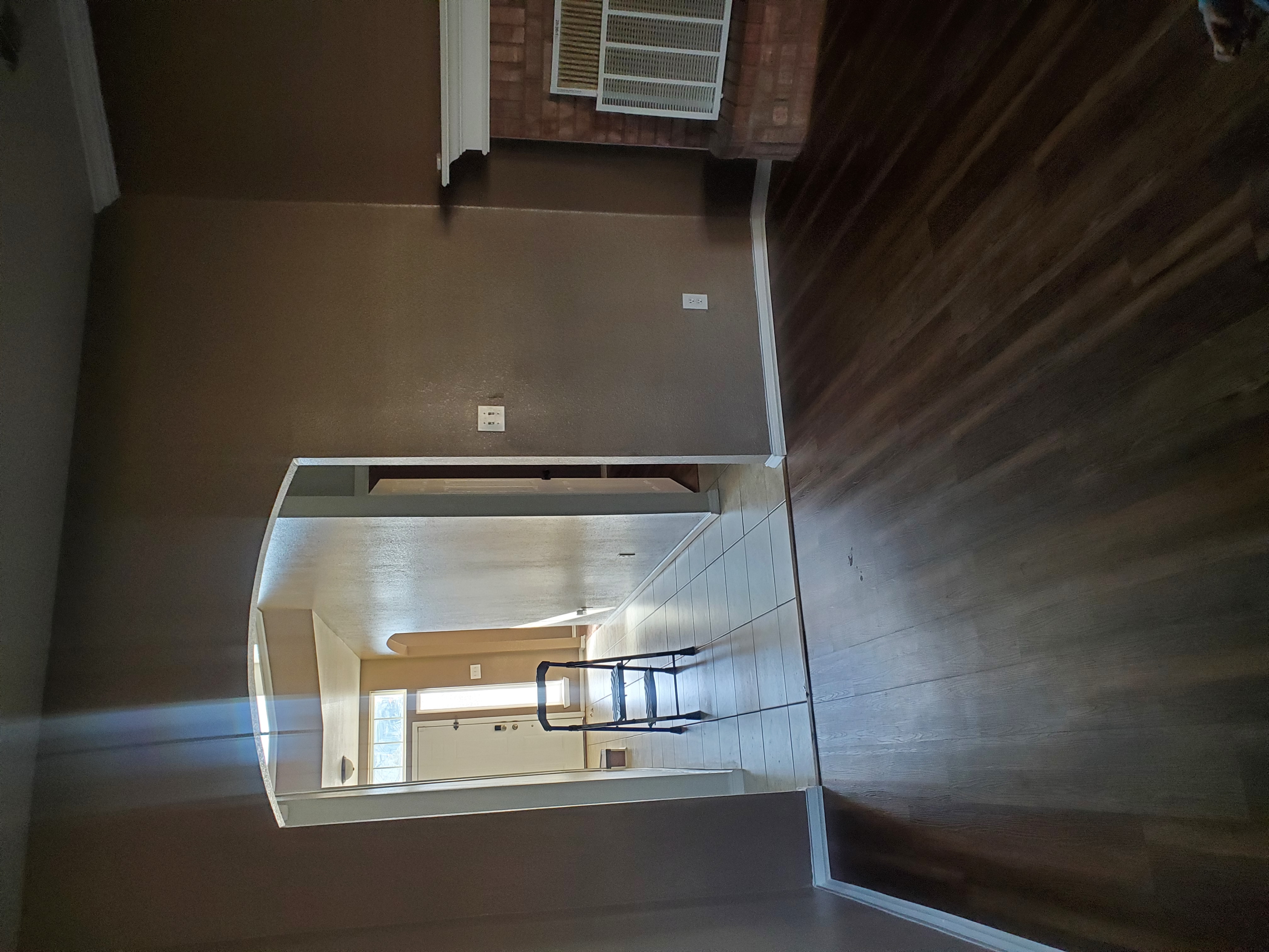 interior shot of a room with dark wood flooring and brown walls. a doorway leads to a tiled entryway where a step stool is placed. a fireplace is visible on the right.