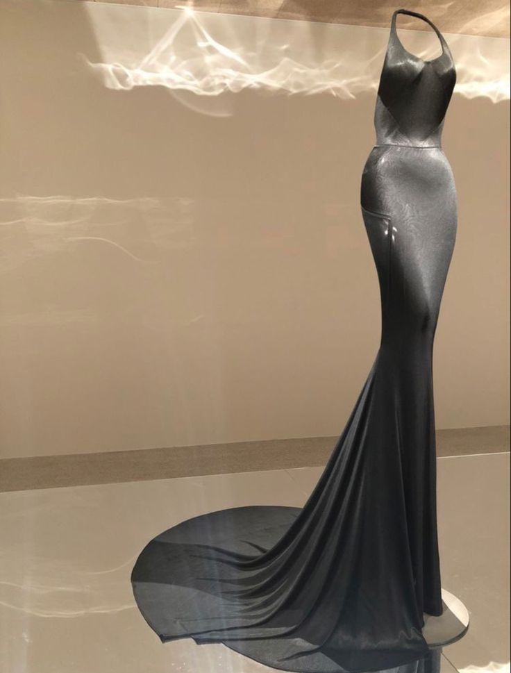 a black, halter neck mermaid style evening gown is displayed on a mannequin. the gown features a fitted bodice and a flared skirt with a train. it is showcased on a reflective surface with distinctive lighting patterns.
