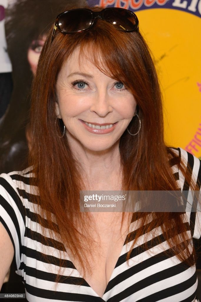 a closeup portrait of a woman with long red hair wearing sunglasses and a black and white striped shirt, smiling at the camera. she is looking at the camera, and her hair is covering most of her face. she is wearing a lowcut shirt that reveals her cleavage. the background is a blurry yellow and white.