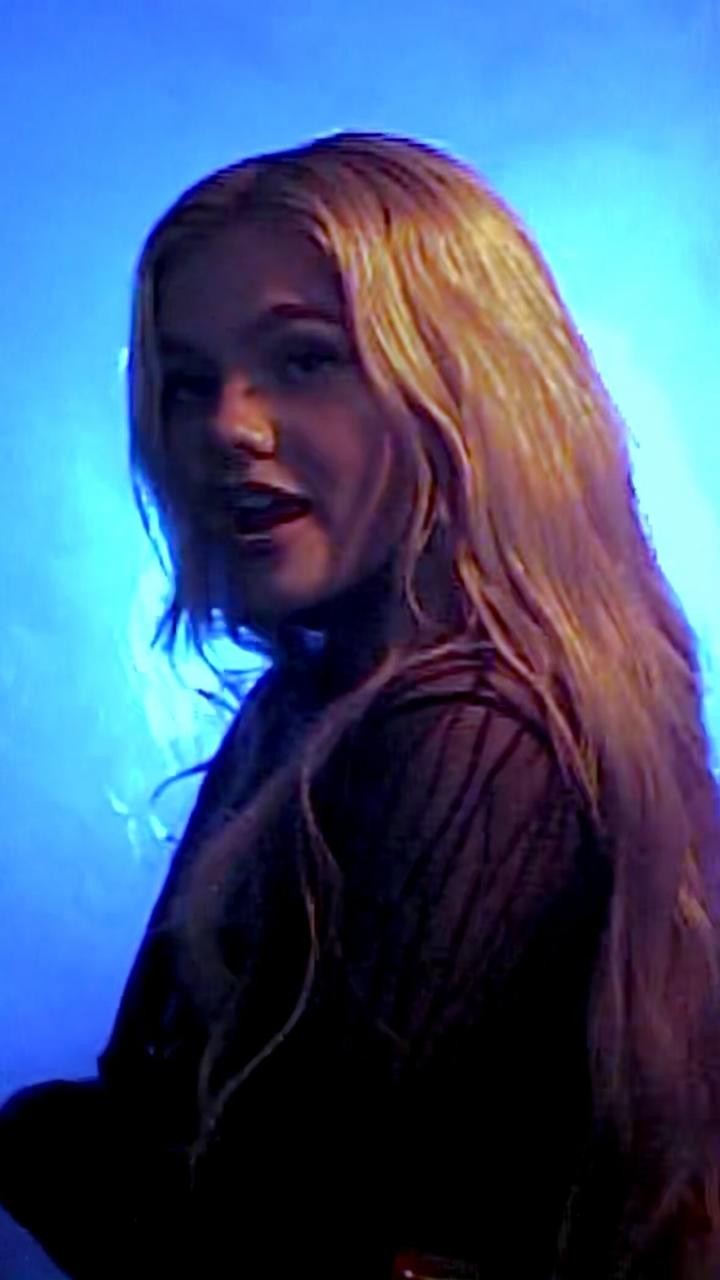a portrait of a blonde woman with her mouth slightly open. she has long hair and is facing towards the left side of the frame. the background is blue.