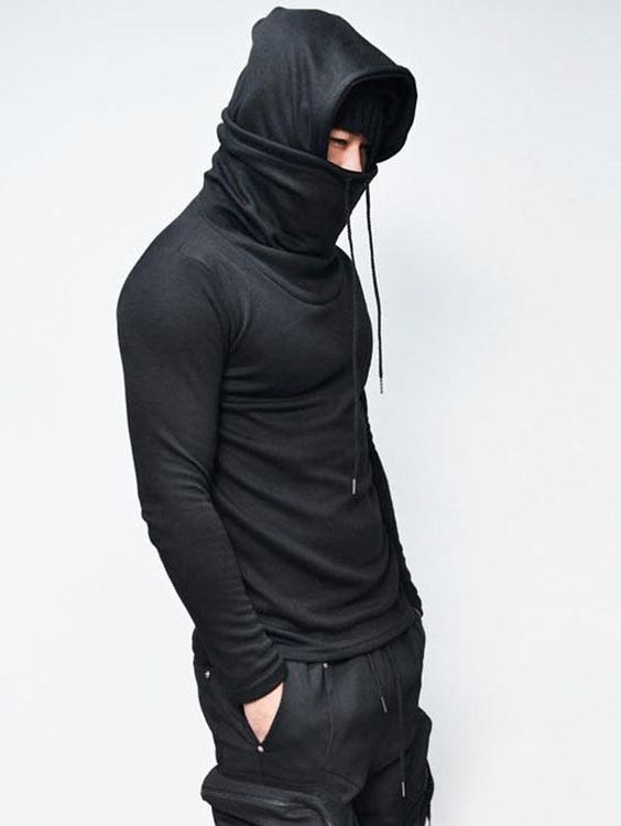 a man stands against a light gray background, modeling a black longsleeved shirt with an integrated turtleneck and hood. the hood is pulled up, partially obscuring his face, and the overall look is sleek and minimalist.