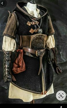 a mannequin is dressed in a medievalinspired outfit, featuring a black hooded tunic, brown leather vest, and various accessories like belts, pouches, and arm guards. the costume is highly detailed with buckles, studs, and fur accents, showcasing a blend of practicality and style. the background is a neutral gray, highlighting the outfit. the lighting is soft, casting subtle shadows and enhancing the texture of the fabrics and leather.