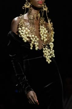 a woman wearing a beautiful black velvet dress accessorized with stunning gold and pearl jewelry. the intricate design of the jewelry features intricate goldwork and clusters of pearls, creating a truly glamorous and elegant look.  the model's dark skin and bold makeup further enhance the overall striking appearance, making her the center of attention.