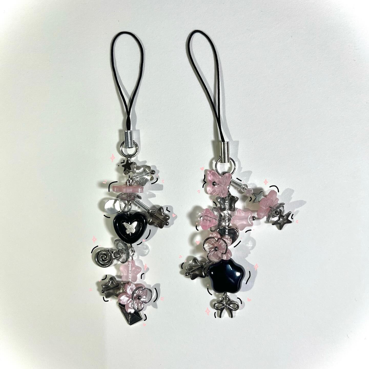 the image shows two handmade cell phone charms with a combination of pink, black, and silver plastic beads in various shapes. the charms feature stars, hearts, flowers, and bows, attached to black string loops for phone attachment. they are on a white background.