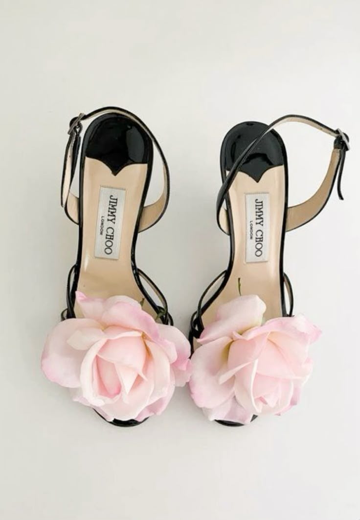 the image shows a pair of jimmy choo high heel sandals with a pink rose embellishment on the toe. the shoes are black patent leather with a delicate ankle strap. the insole is a light beige color and features the "jimmy choo london" logo. they are presented against a plain white background.